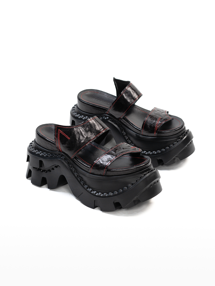 Engineered with a bold industrial attitude, these platform leather slides deliver a powerful fusion of structure and street-ready design. Crafted from glossy black leather and accented with sharp red contrast stitching, the upper introduces a raw, deconstructed edge. The exaggerated sculpted outsole adds height and impact, creating a silhouette that feels both aggressive and refined. Designed for modern wardrobes that blur the line between utility and fashion, this pair makes an effortless statement.
